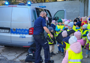 Pan policjant ubiera dzieci w kamizelkę ochronną i kask