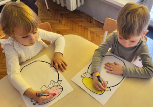 dwoje dzieci siedzi przy stoliku i kolorują duży słoik
