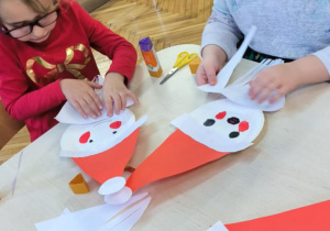 Dziewczynka przykleja na papierowy talerzyk brodę Mikołaja