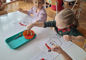 Dziewczynki maczają gąbeczki w czerwonej farbie