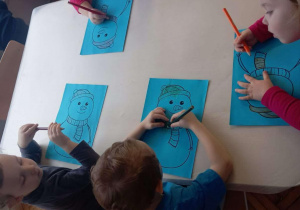 Dzieci przy stoliku kolorują czapki bałwankom