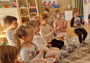 dzieci siedząc na krzesłach grają na instrumentach