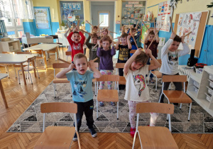 dzieci stoją za krzesłami grajac na instrumentach