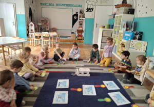 Dzieci siedzą na dywanie przed ilustracjami zimowymi