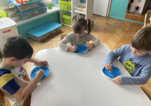 Dzieci białą kredką malują na niebieskim tle