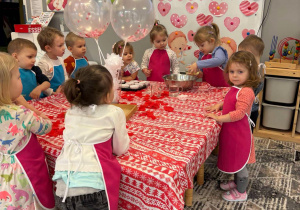 Dziewczynka wlewa do miski olej a reszta dzieci stoi przy stole