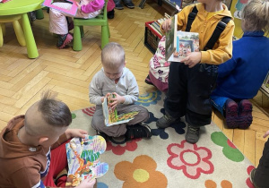 Dzieci siedzą na dywanie i oglądają książeczki