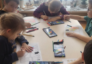 Dzieci przy stole koloruja kartę pracy z rakietami