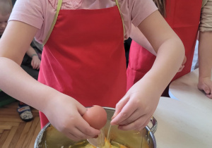 Dziewczynka wbija jajko do miski z masą na pączki
