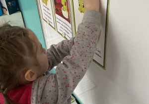 Dziewczynka przyczepia ilustracje z historyjką obrazkową o dinozaurze