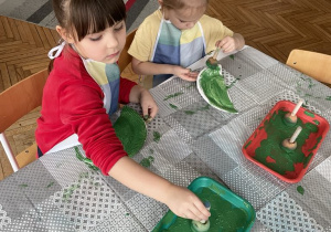 Dziewczynki przy stole malują na zielono talerzyk papierowy