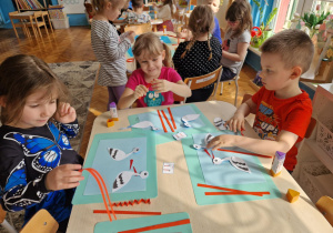 Dzieci wycinają czerwone paski jako nogi bociana