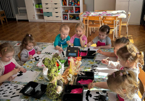 Cała grupa dzieci siedzi przy stole i maluje łatki krowy