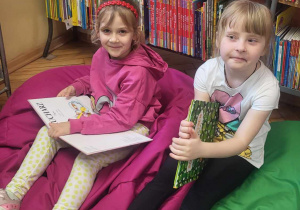 dwoje dzecii siedzi na poduchacch, trzymając w rękach ksiąki