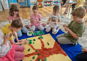 dziecie siedząc wokół maty na dywanie, układają sylwetę drzewa z bibuły
