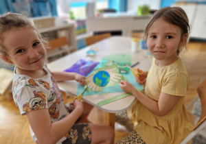 dwie dziewczynki siedzą i pozują do zdjęcia podczas wwykonywania pracy plastycznej
