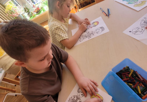 Dzieci przy stole kolorują stroje regionalne