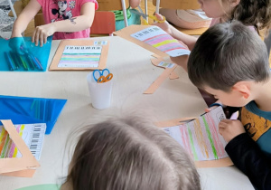 Dzieci kolorują i wycinają przy stoliku kartę pracy