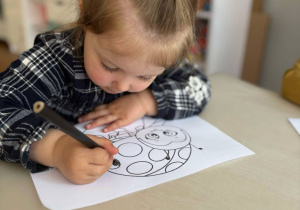 Dziewczynka koloruje przy stoliku biedronkę