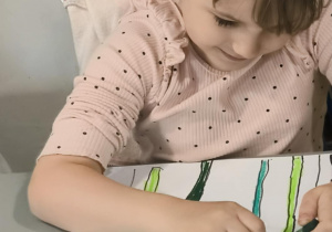 Dziewczynka koloruje na zielono łodygi kwiatów