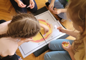 Dzieci ukladaja papierowe produkty na pizzy