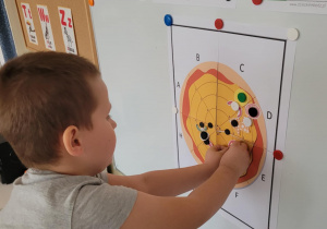 Chlopiec przyczepia na papierowej pizzy papierowego pomidora