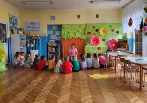 dzieci siedzą przed zakrytą tablicą i paną Beatką