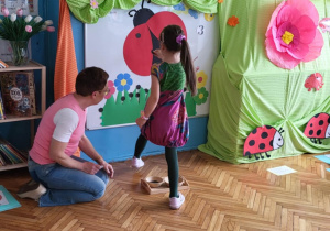 dziewczynka rozwiązuje zadanie matematyczne stojąc rzed tablicą, na której widać dużą biedronkę