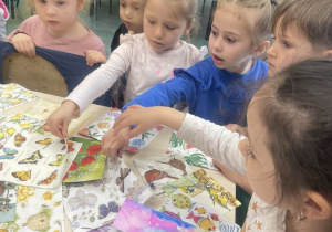 dzieci stojąc przed stolikiem wybierają kartki ze wzorami do pracy plastycznej