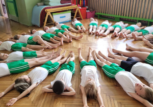 Dzieci leżą na plecach na sali gimnastycznej
