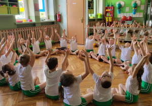 Dzieci wyciągają ręce w górę w pozycji siadu