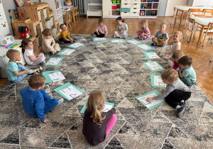 Dzieci siedza w kole z kartami pracy i patyczkami