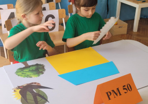 Dziewczynka układa płotek po lewej stronie domku