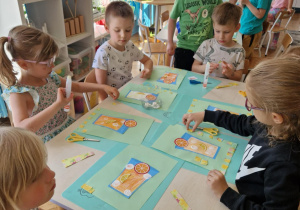 Dzieci przykeljają na szablon szklanki papierowe cytryny i pomarańcze