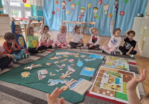 Dzieci siedza na dywanie przed ilustracjami wakacyjnymi