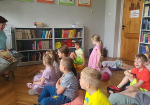 Dzieci słuchają czyatnej przez panią bibliokekarkę książki