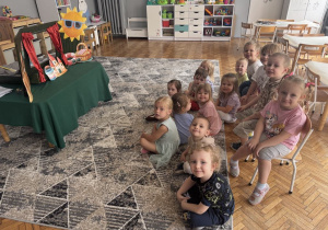 Dzieci siedzą na krzesłach przed teatrzykiem