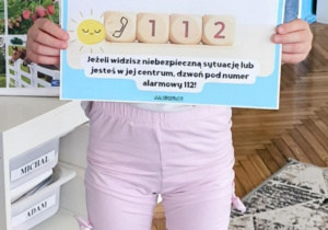 Dziewczynka pokauje plansze z numerem 112
