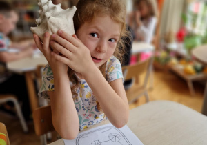 Dziewczynka przykłada do ucha wielką muszlę