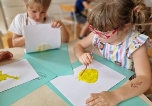 Dziewczynki dmuchaja na żółtą farbę przez słomkę