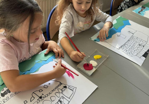 Dziewczynki nabierają czerwoną farbę na pędzle