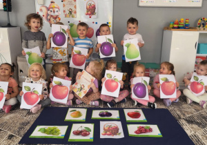 dzieci z grupy pierwszej pozują do zdjęcia z ilustracjami owoców