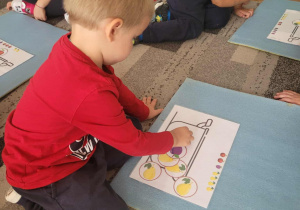 Chłopiec uklada ilustracje owoców na szablonie garnka