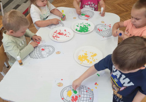 Dzieci przy stoliku wyklejają kosz z owocami