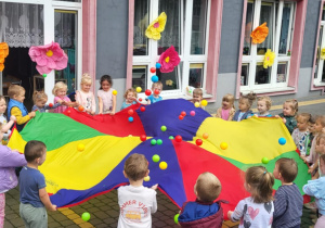 dzieci stoją wokół chust animacyjnych i podrzucają na nich pileczki