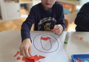 Chłopiec drze czerwony papier na kawałki