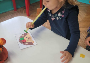 Dziewczynka za pomocą rurki i powietrza przenosi liście
