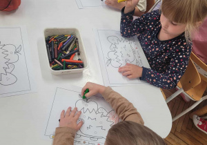Dzieci przy stoliku kolorują kartę pracy