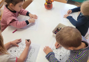 Dzieci przy stoliku kolorują na odpowiednie kolory kartę pracy z jeżykiem