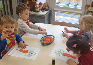 dzieci wykonuja pracę plastyczną klejąc pomarańczową bibułę